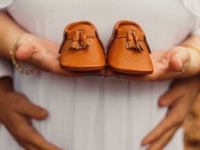Pregnant woman holding a pair of brown baby shoes Pregnant woman holding a pair of brown baby shoes