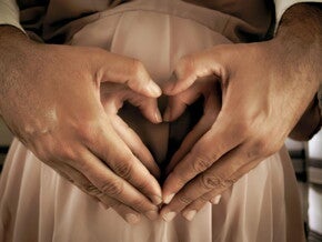 Couple holding hands in the shape of a heart over a pregnant belly Couple holding hands in the shape of a heart over a pregnant belly