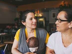 Woman with baby in carrier talking to an older woman Woman with baby in carrier talking to an older woman