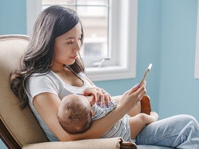 Woman sitting on couch holding her sleeping baby while on the phone Woman sitting on couch holding her sleeping baby while on the phone