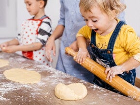 toddlers rolling out dough in the kitchen to cook