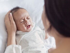 Crying baby in white being comforted by their parent Crying baby in white being comforted by their parent