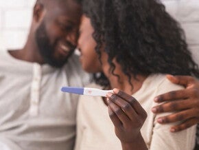 Couple hugging while holding a positive home pregnancy test Couple hugging while holding a positive home pregnancy test