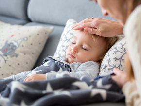 Toddler laying down with mothers hand on toddlers head