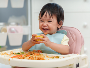 Toddler girl holding corn on a messy highchair Toddler girl holding corn on a messy highchair