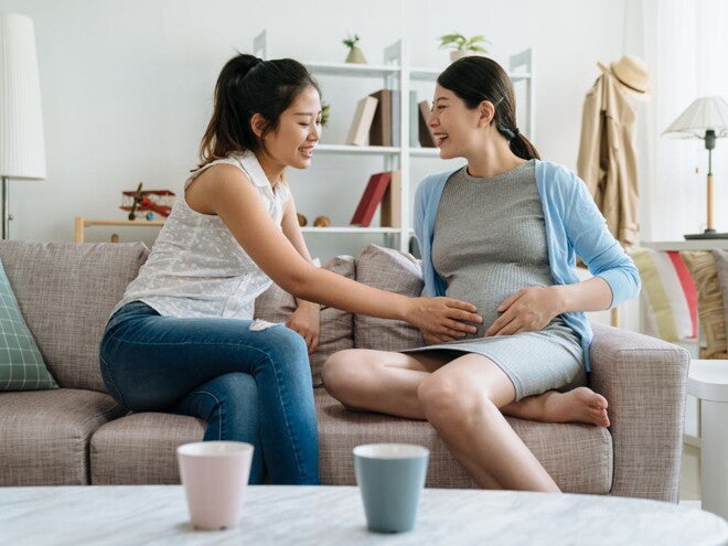 Pregnant woman and friend touching her belly