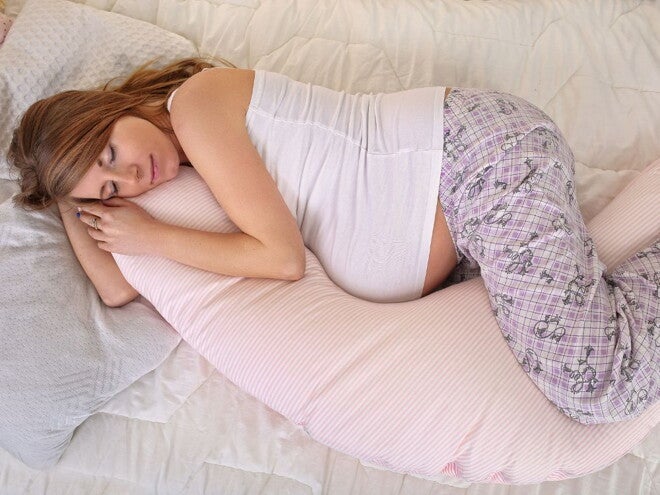 Pregnant woman lying on a bed with pregnancy pillow Pregnant woman lying on a bed with pregnancy pillow